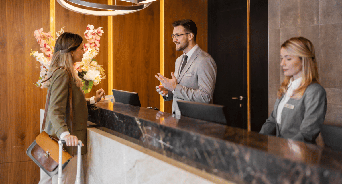 Guest with suitcase at hotel font desk with hotel staff attending to guest