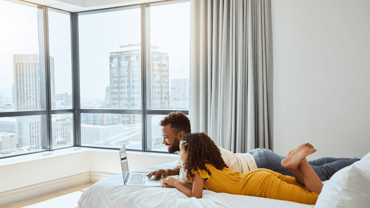 Dad and daughter laying on hotel bed staring at laptop