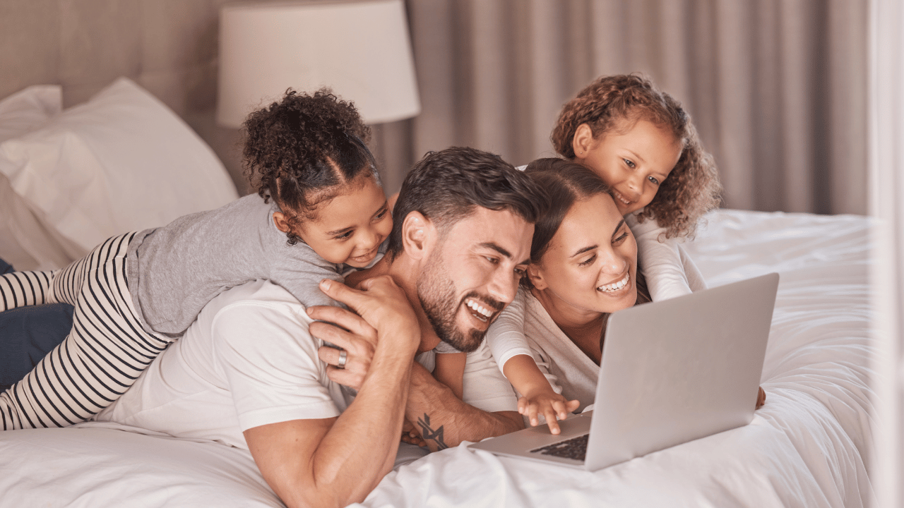 Family laying on hotel bed staring at laptop